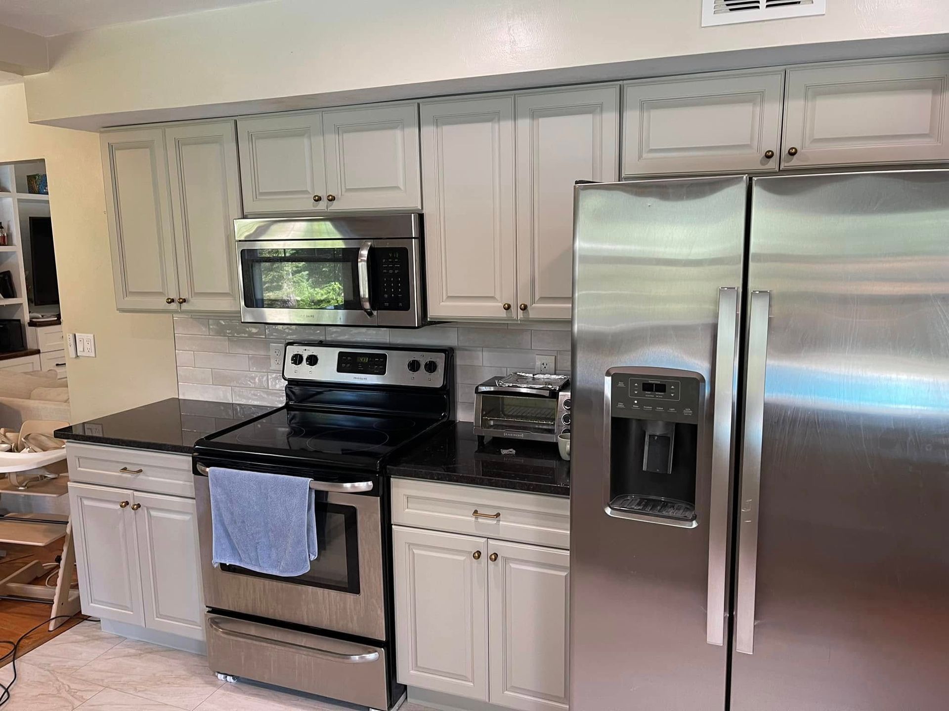 Kitchen with stainless steel appliances, light cabinets, black countertops, and a white backsplash.