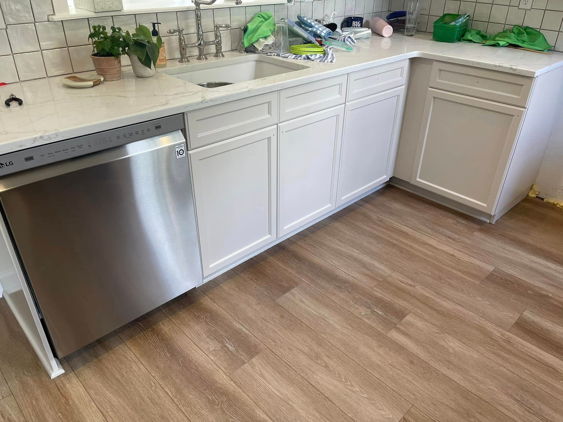 Stainless steel dishwasher, white cabinets, and light wood-look flooring in a kitchen.