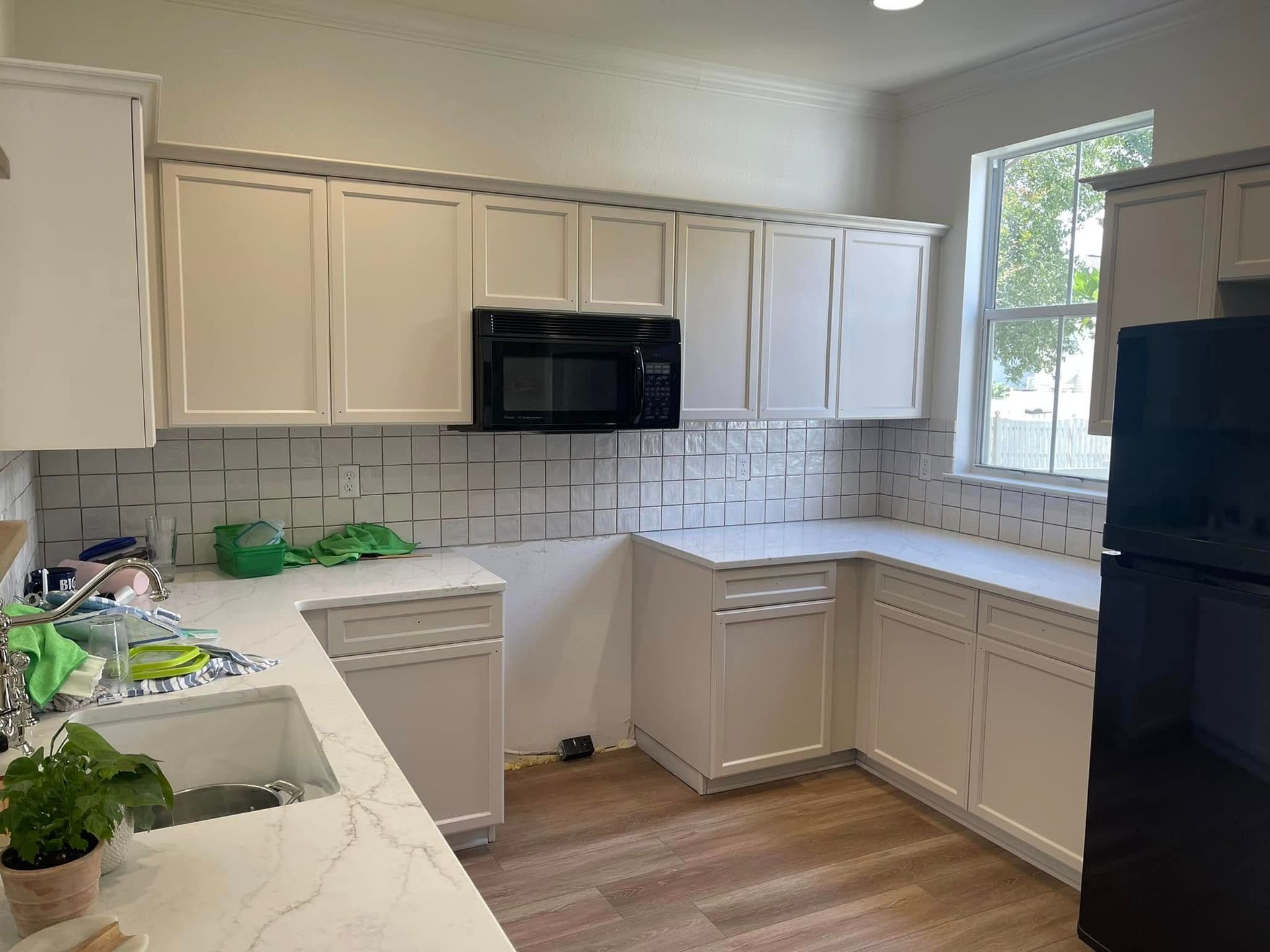 White kitchen with cabinets, countertops, and backsplash. Includes black microwave and refrigerator.
