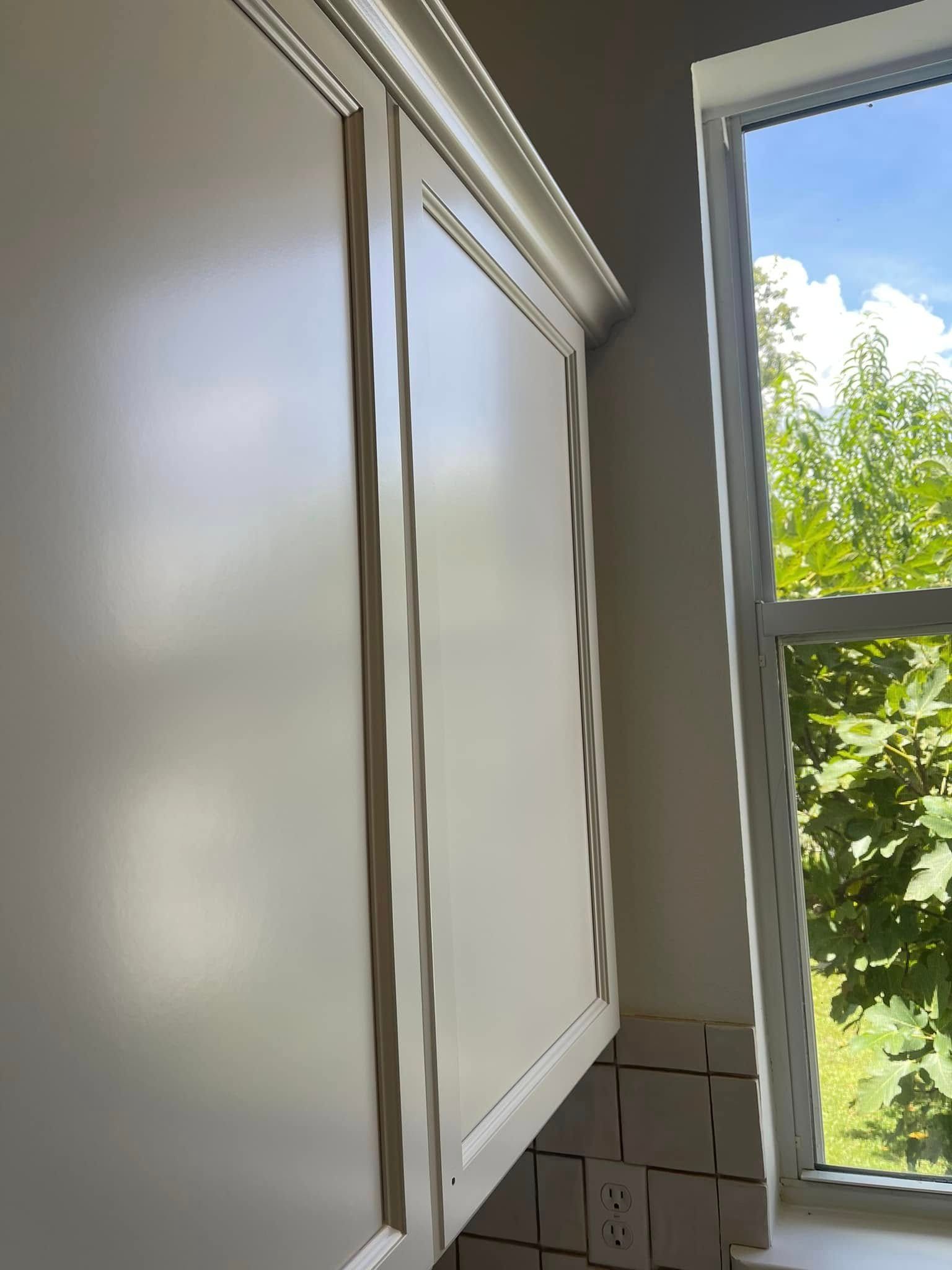 Cream-colored kitchen cabinets next to a window with a view of green trees.