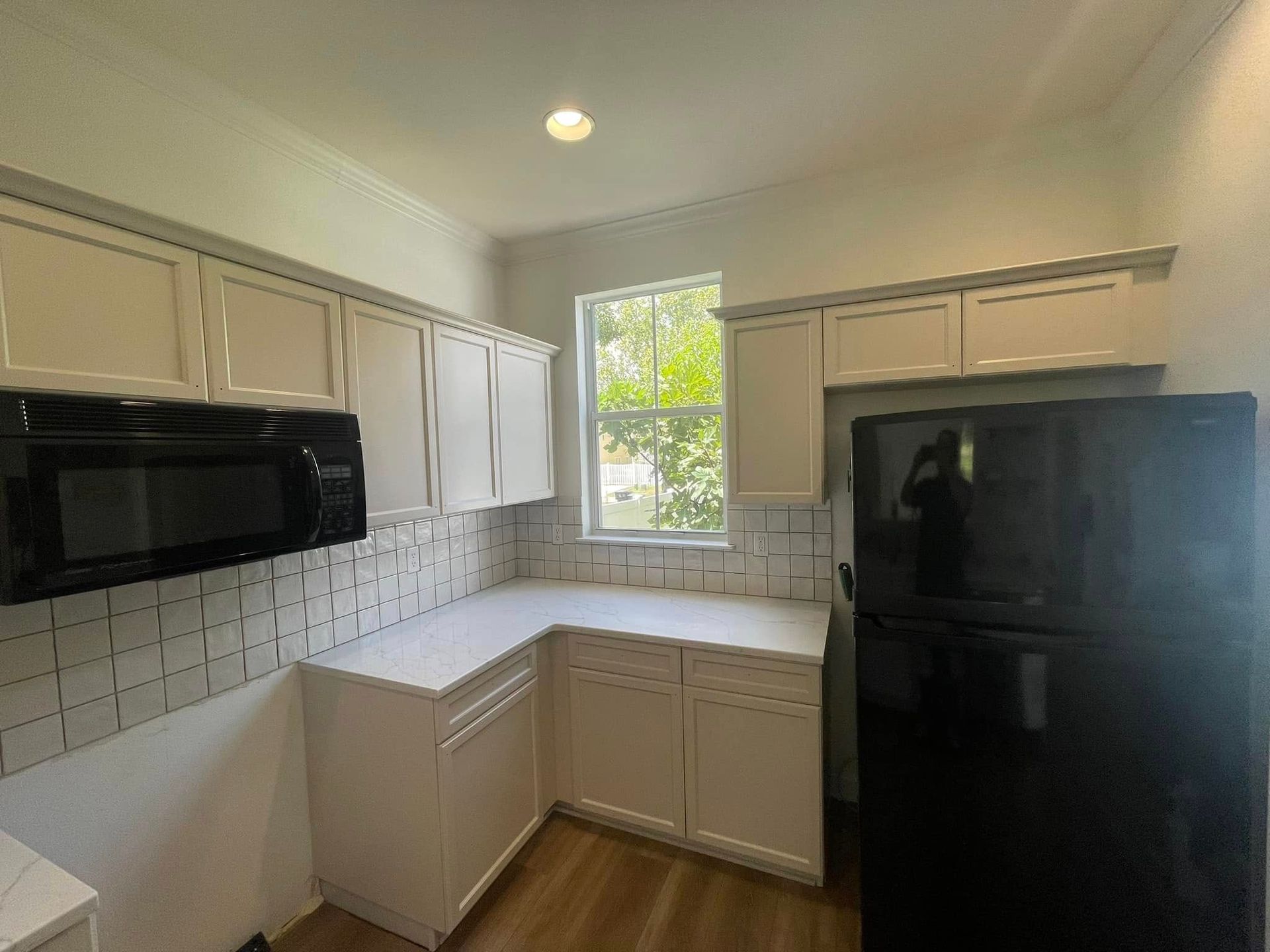 Small kitchen with white cabinets, subway tile backsplash, black appliances, and a window.