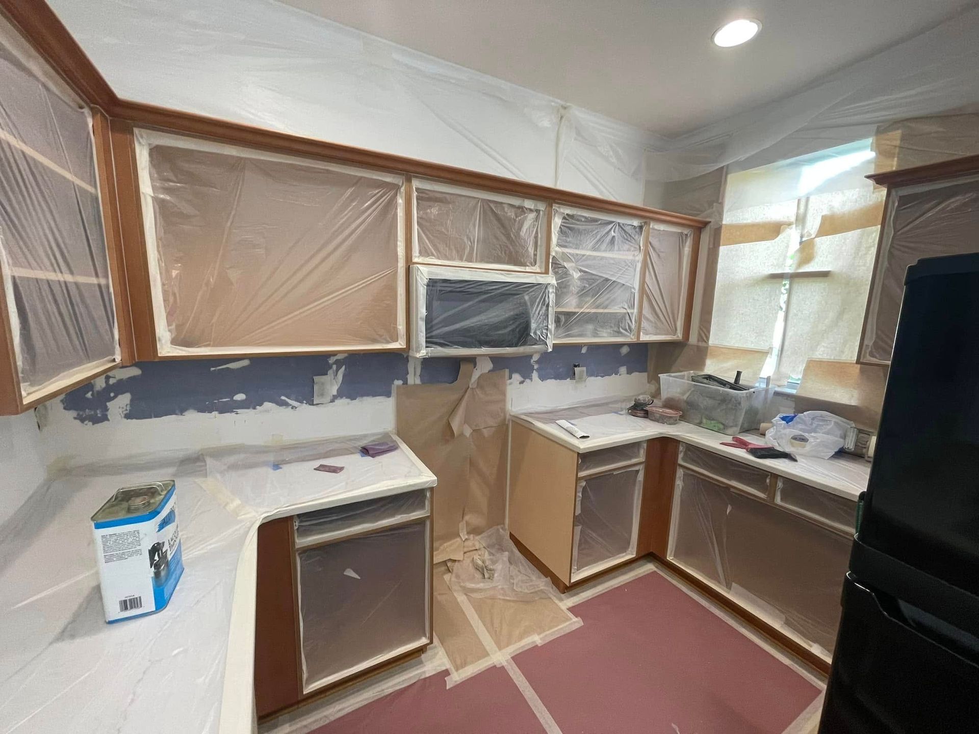 Kitchen renovation in progress: cabinets covered in plastic, walls prepped for painting, countertops masked.