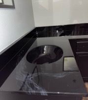 Black countertop with a circular sink, reflective surface, near a white wall.
