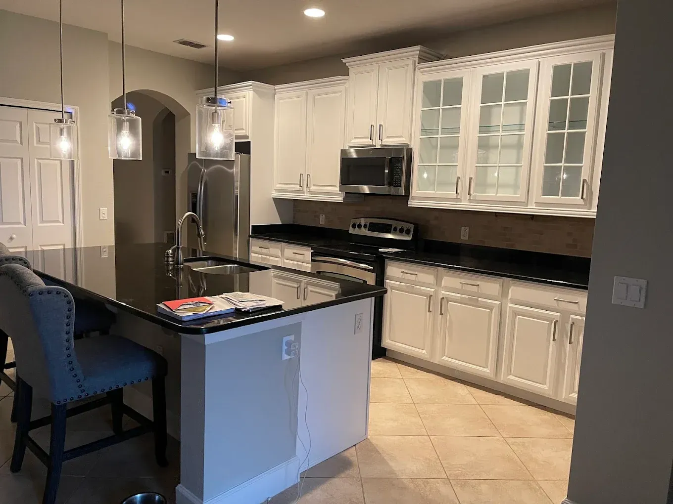 Modern kitchen with white cabinets, black countertops, stainless steel appliances, and a dark island.