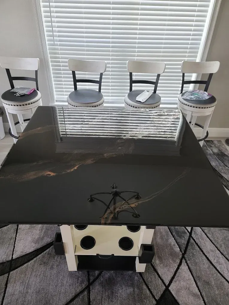 Black and gold resin table with four stools, near window with blinds.