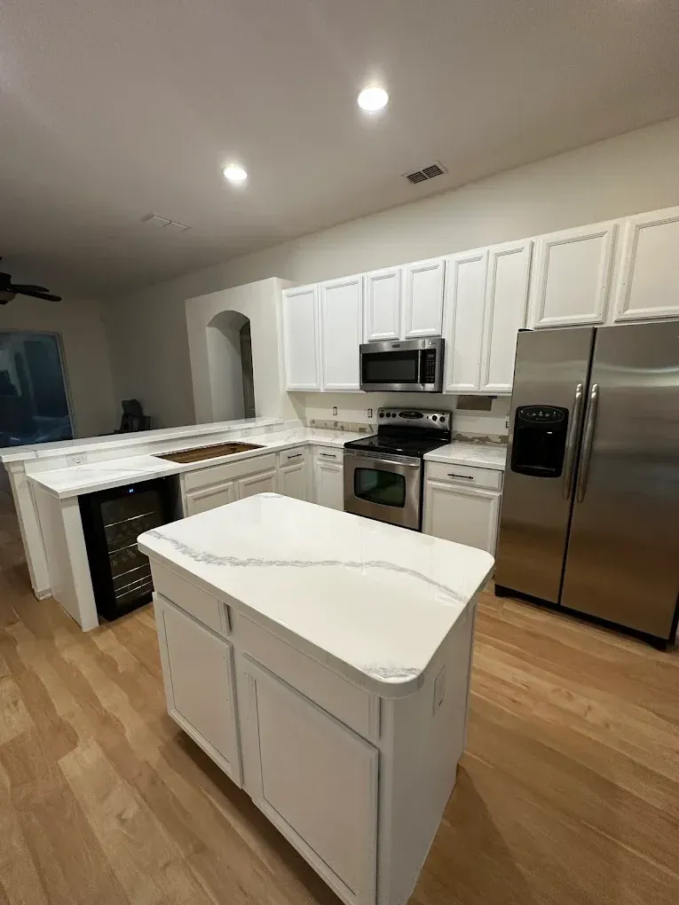 White kitchen with island, stainless steel appliances, and light wood floors.