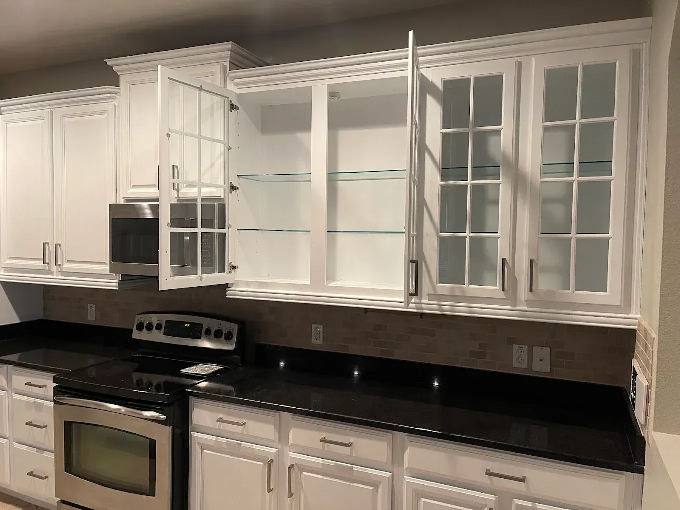 White kitchen cabinets with a black countertop and a stainless steel stove and microwave.