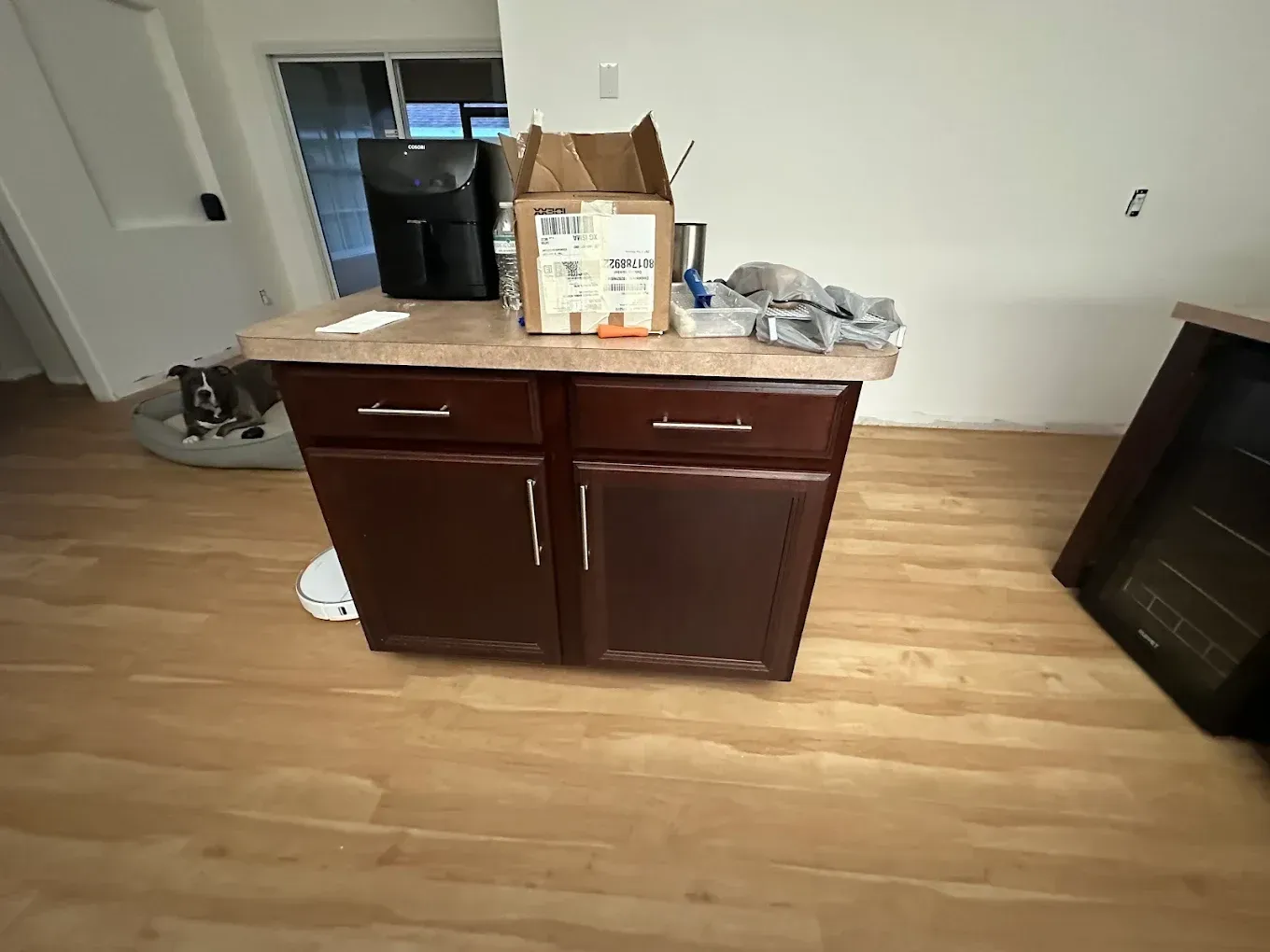 Kitchen island with cabinets, cardboard box, appliances, and a window in the background.