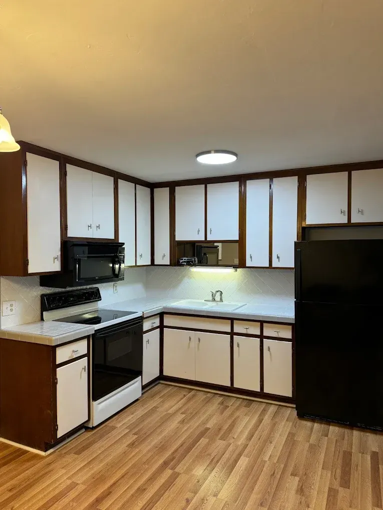 Kitchen with white and brown cabinets, black appliances, and wood-look floor.