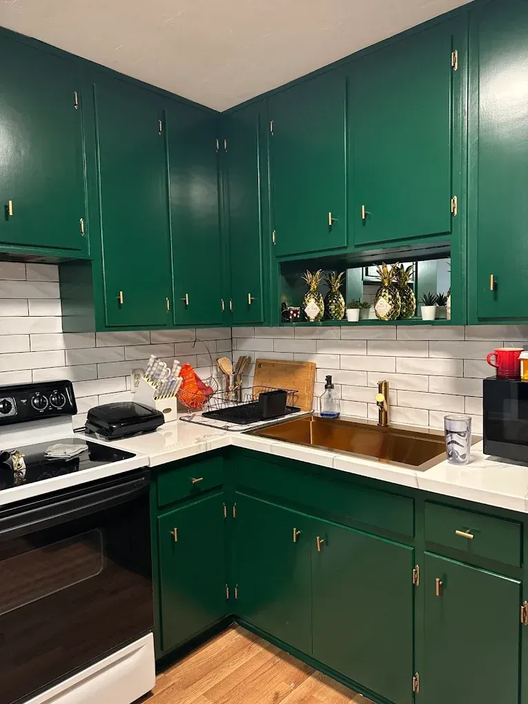 Green kitchen cabinets with white backsplash and gold hardware.