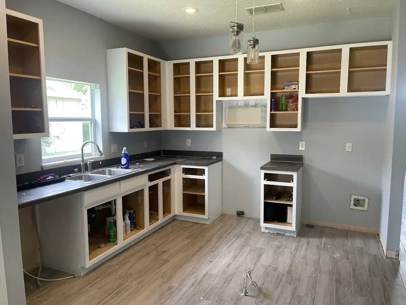 Kitchen with gray walls, white cabinets, dark countertops, and light wood-look flooring.