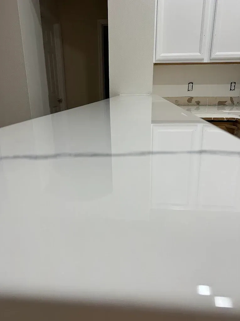 White countertop with a reflective surface, near white cabinets and a door.