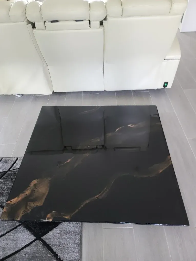 Black and gold marbled coffee table in front of a white recliner sofa on a gray tiled floor.