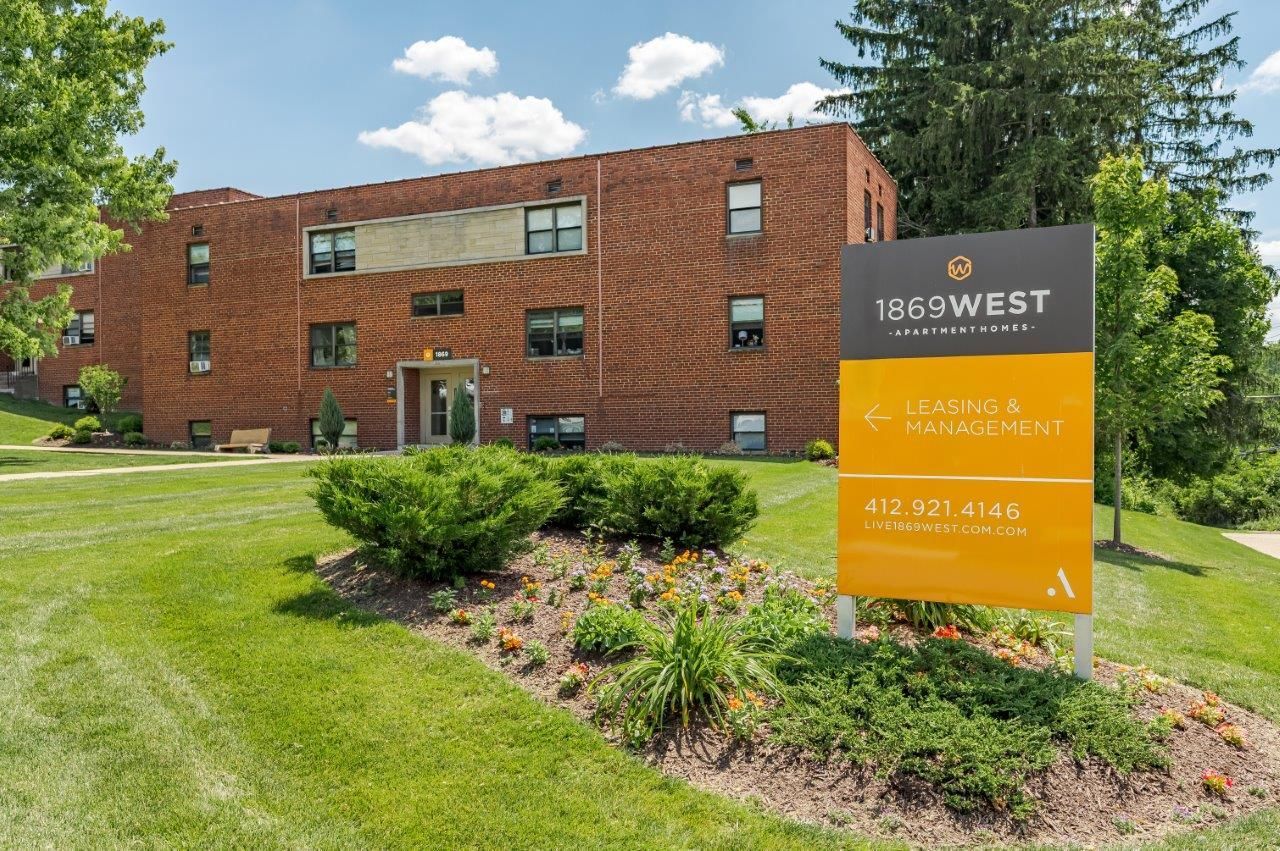 Brick office building with a 169West sign, green lawn, and trees on a sunny day