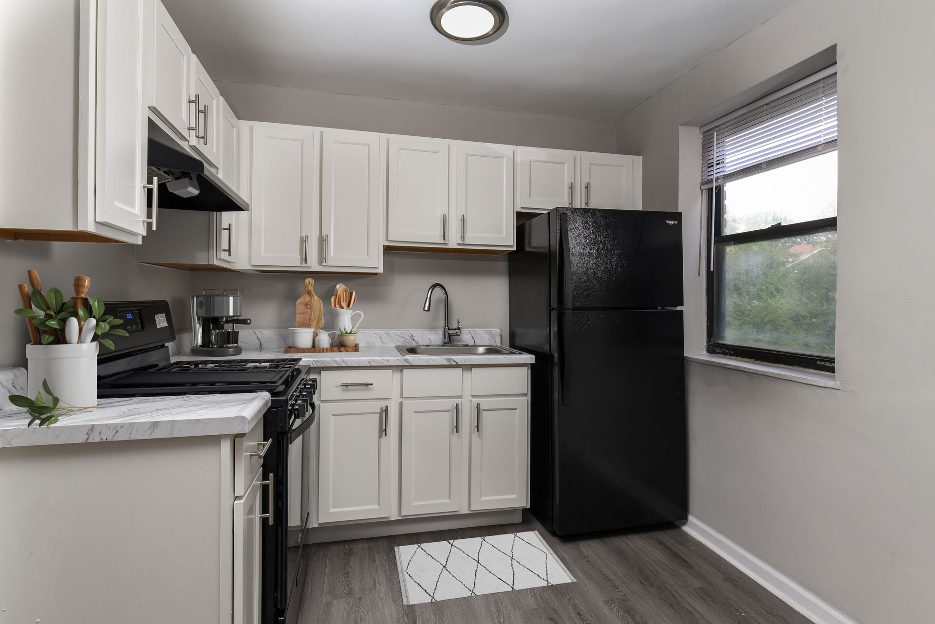 Kitchen with white cabinets, black appliances, and a window with blinds.