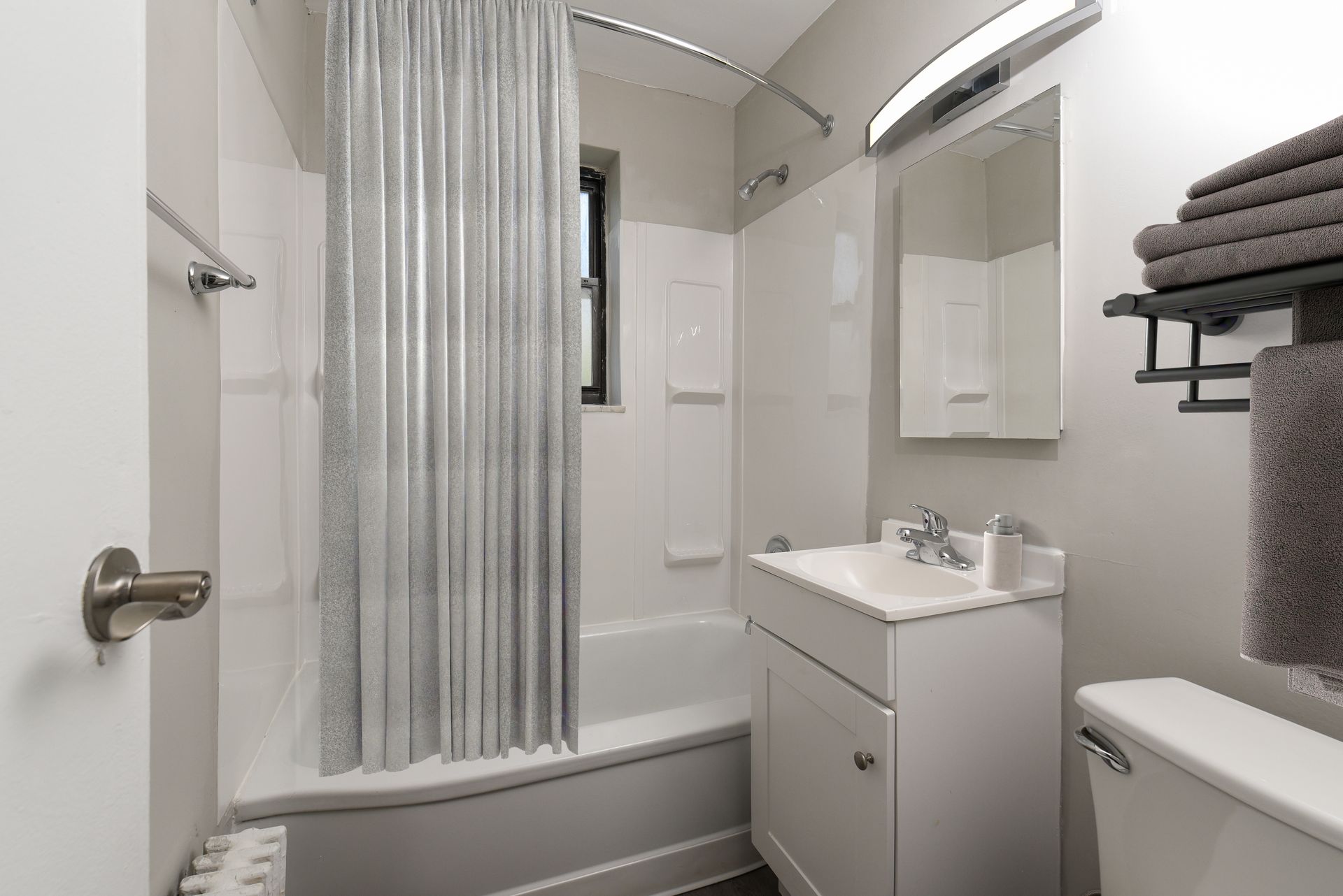 Small white bathroom with a tub, toilet, and sink. Silver shower curtain and gray towels.
