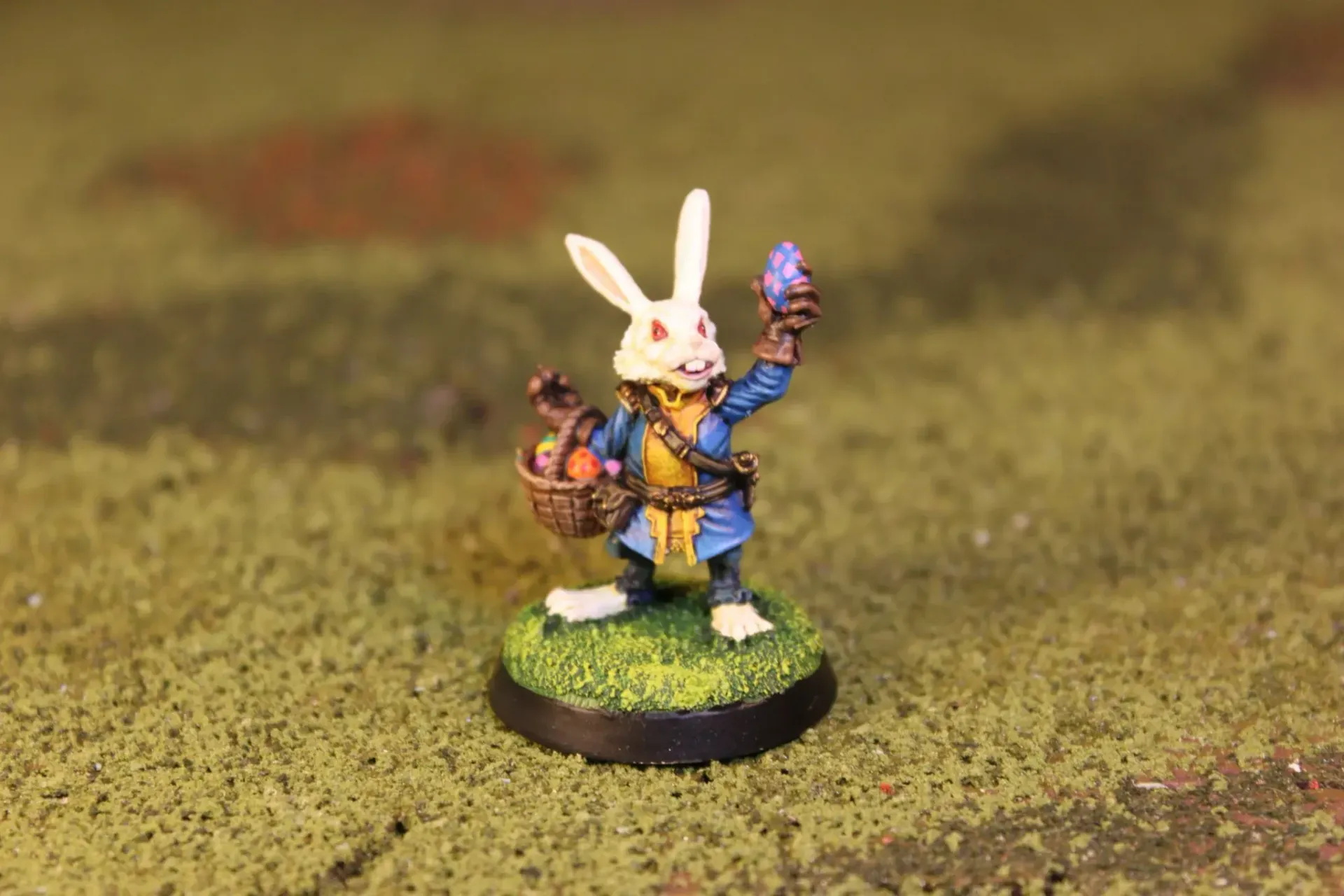 A miniature rabbit character in blue coat, holding a basket and purple egg, on a grassy base.
