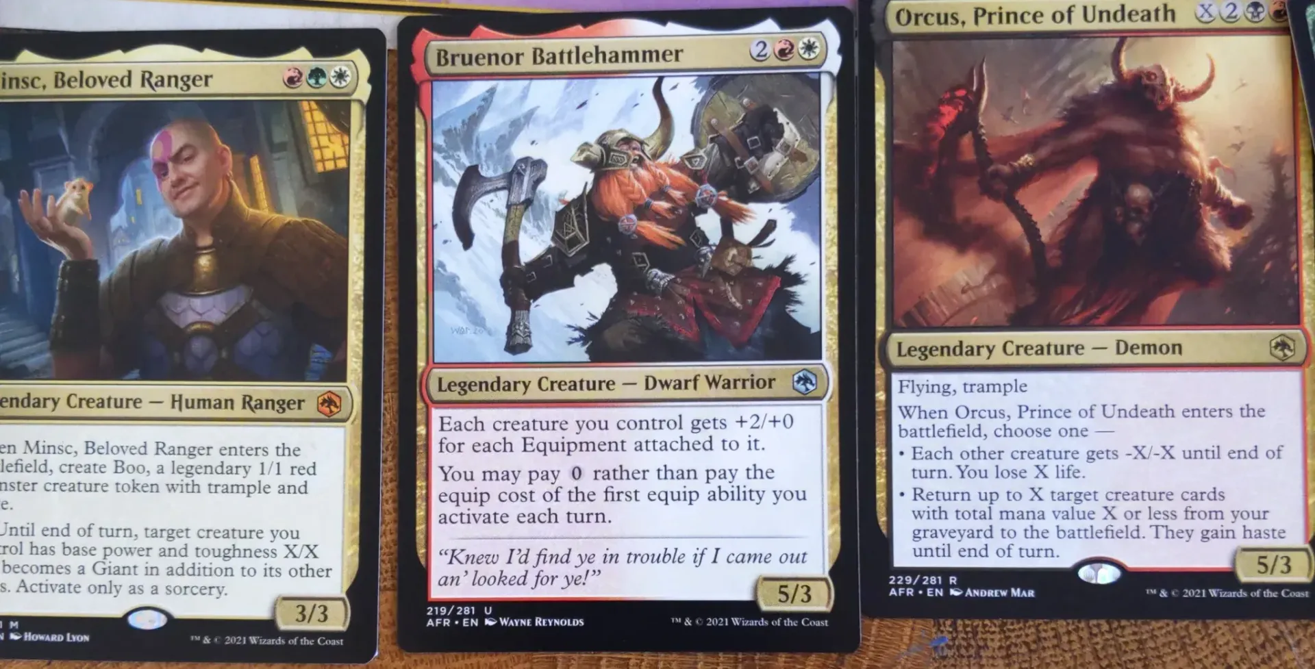 Three Magic: The Gathering cards. A man in a blue setting, a dwarf with axes, and a demon-like creature.