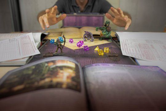 Person playing tabletop role-playing game, hands above miniatures on a map, books open on either side.