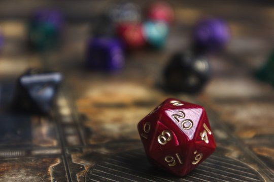 Red d20 die, showing 20, on a game board with blurred dice in the background.