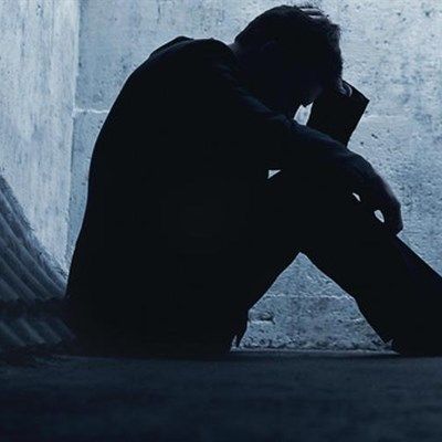 Silhouette of a person sitting alone, head in hand, in a dark, confined space.