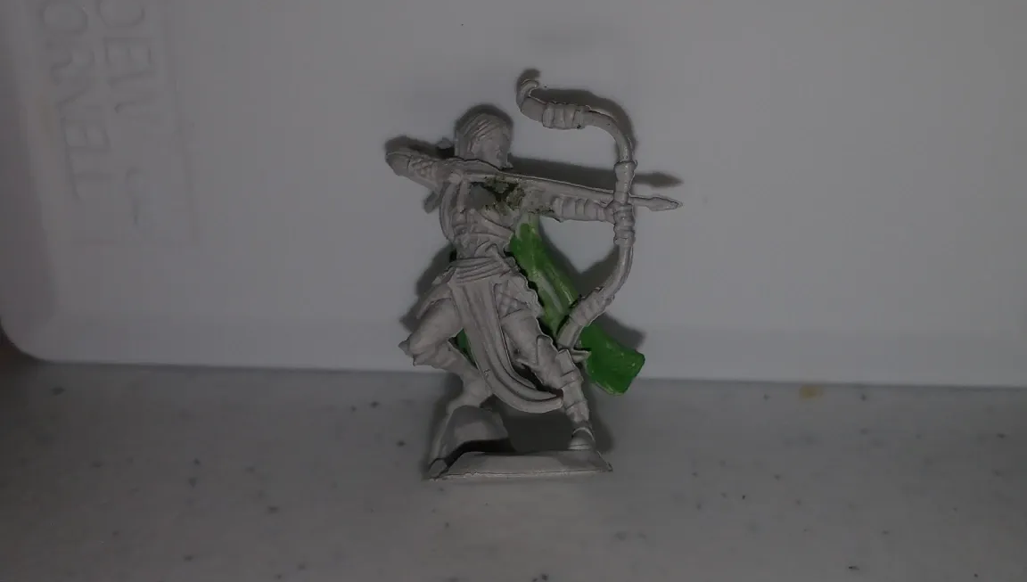 Miniature archer figurine, metallic with a bow drawn. Green foliage base on white surface.