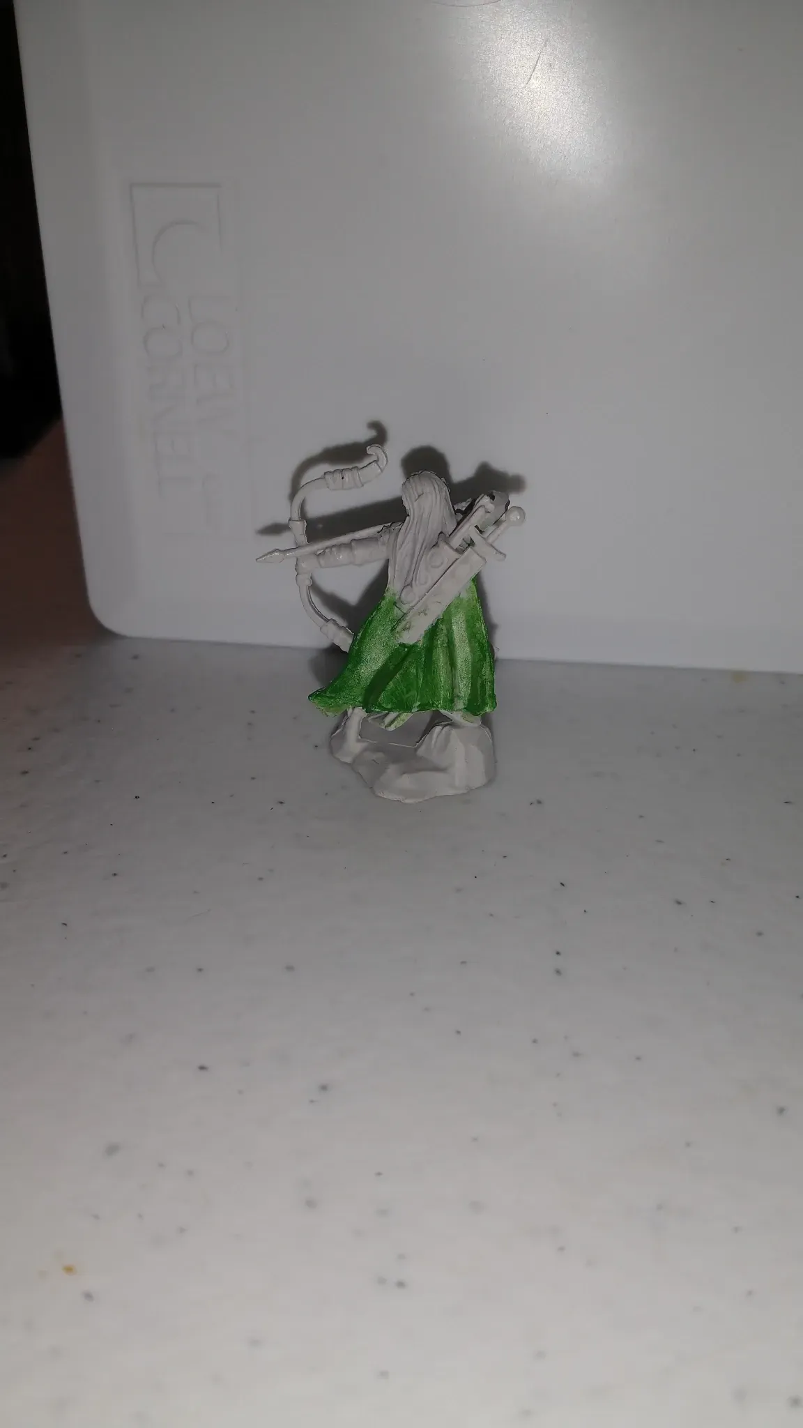A small painted figurine of a woman with bow and arrow; green dress, white skin, white background.
