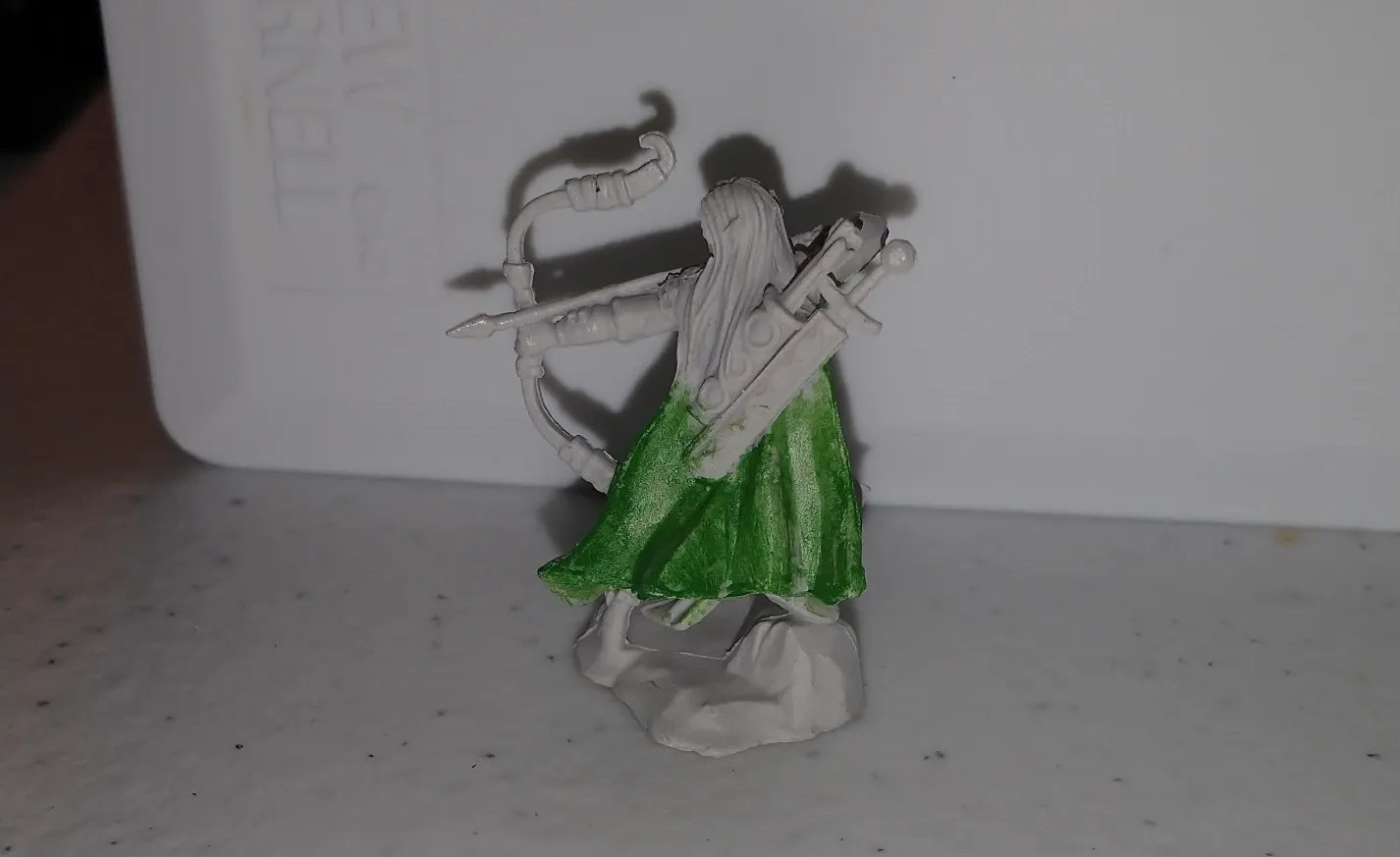 Miniature figure of an archer with a bow and arrow; green clothing, white background.