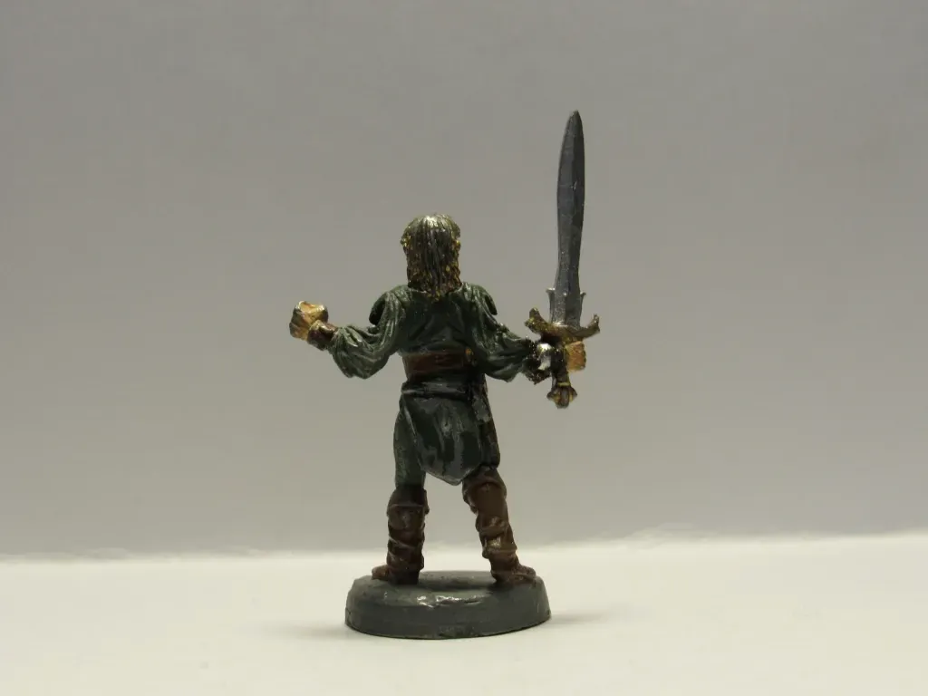 Miniature figure of a warrior, holding a sword and a small object in front of a white background.
