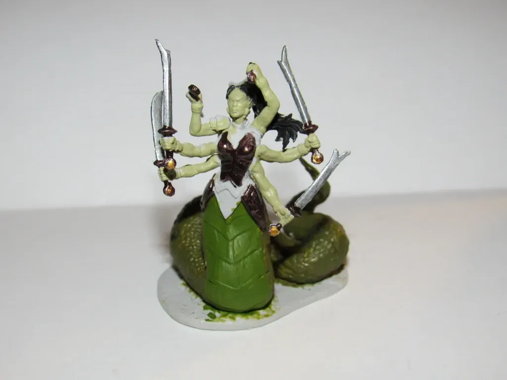 Miniature of a multi-armed, green-skinned snake-like creature holding swords. Brown bodice, dark hair, and a green tail.
