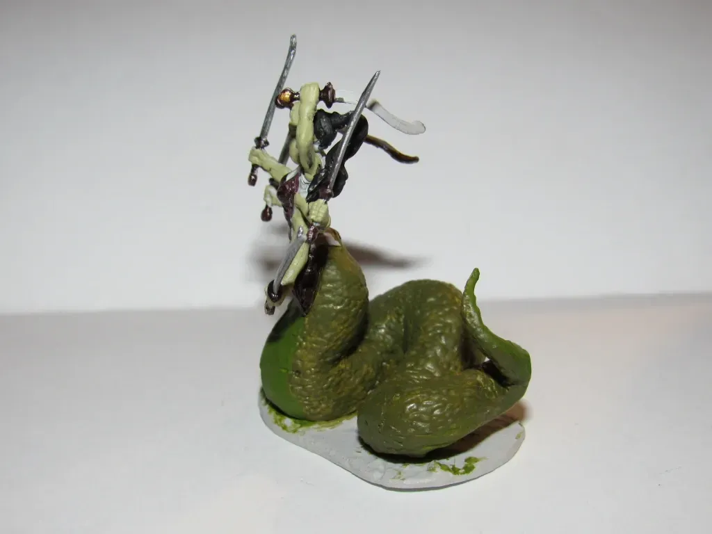 Miniature figure of a serpent with a warrior on its back, holding swords. Green and black tones.