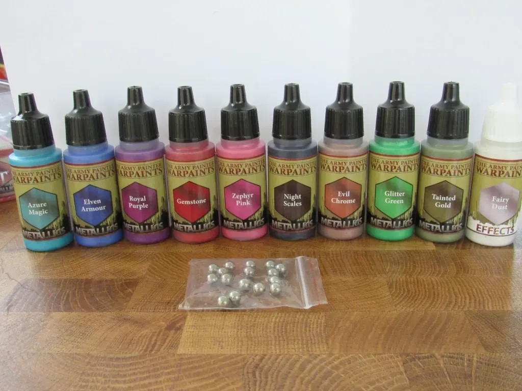 Bottles of ink in various colors, plus a small bag of metal ball bearings, on a wooden surface.
