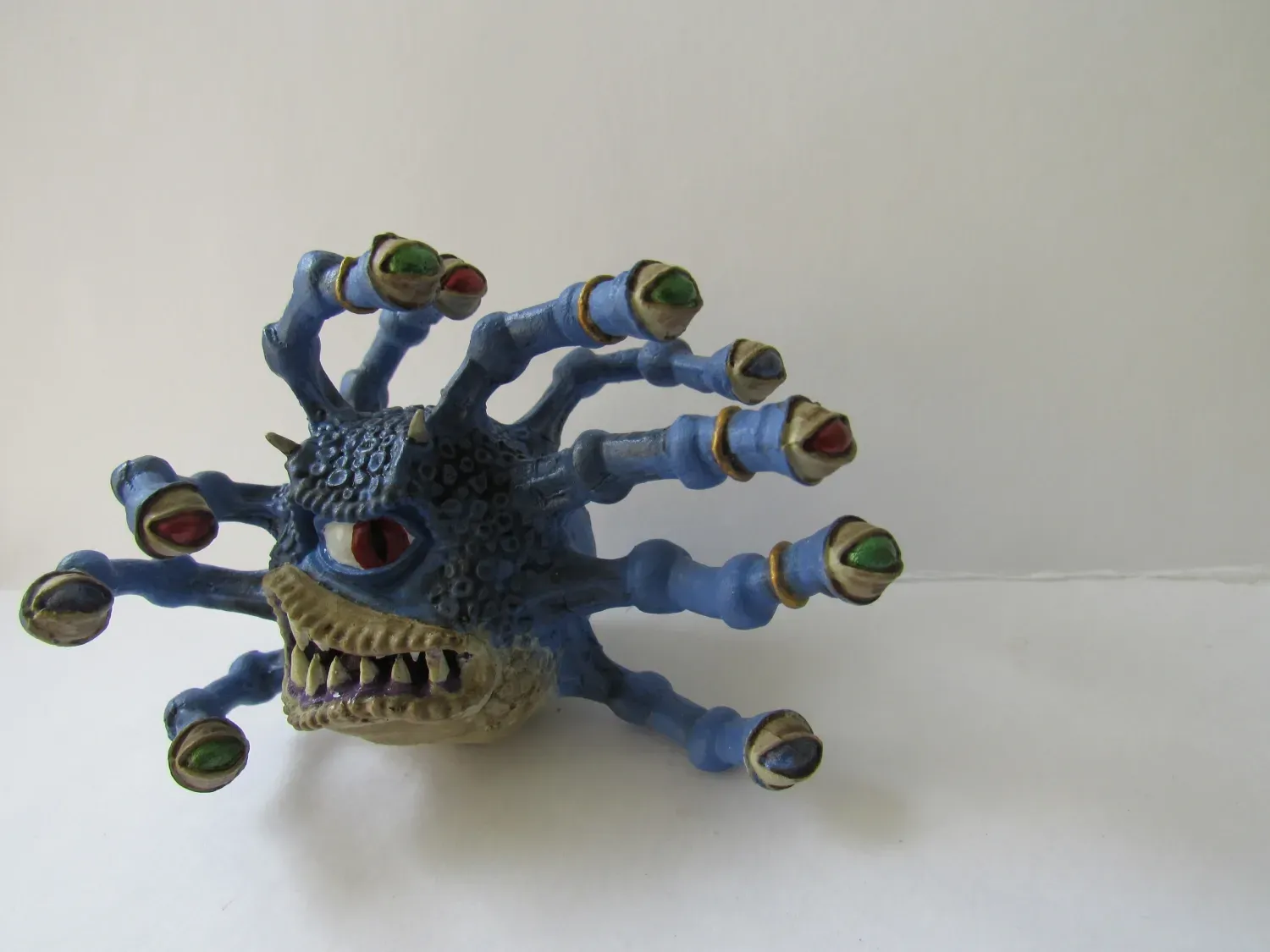 Blue, multi-eyed Beholder toy with sharp teeth, on a white surface.