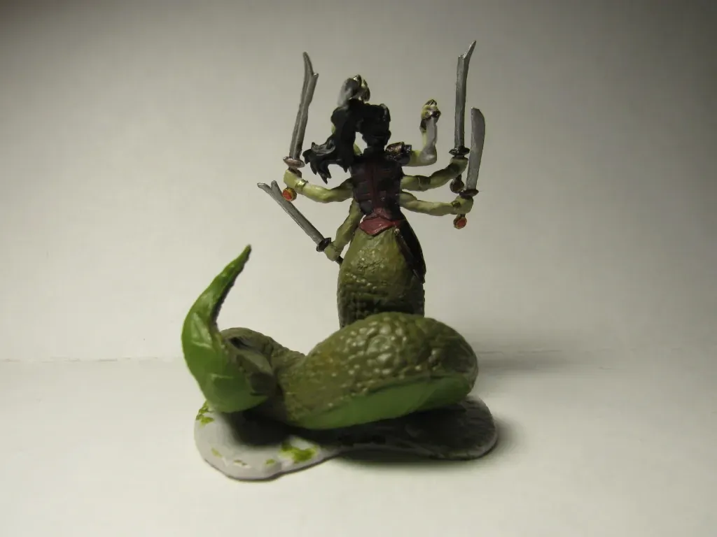 A painted miniature of a multi-armed snake woman holding swords, rising over a green, coiled serpent body.
