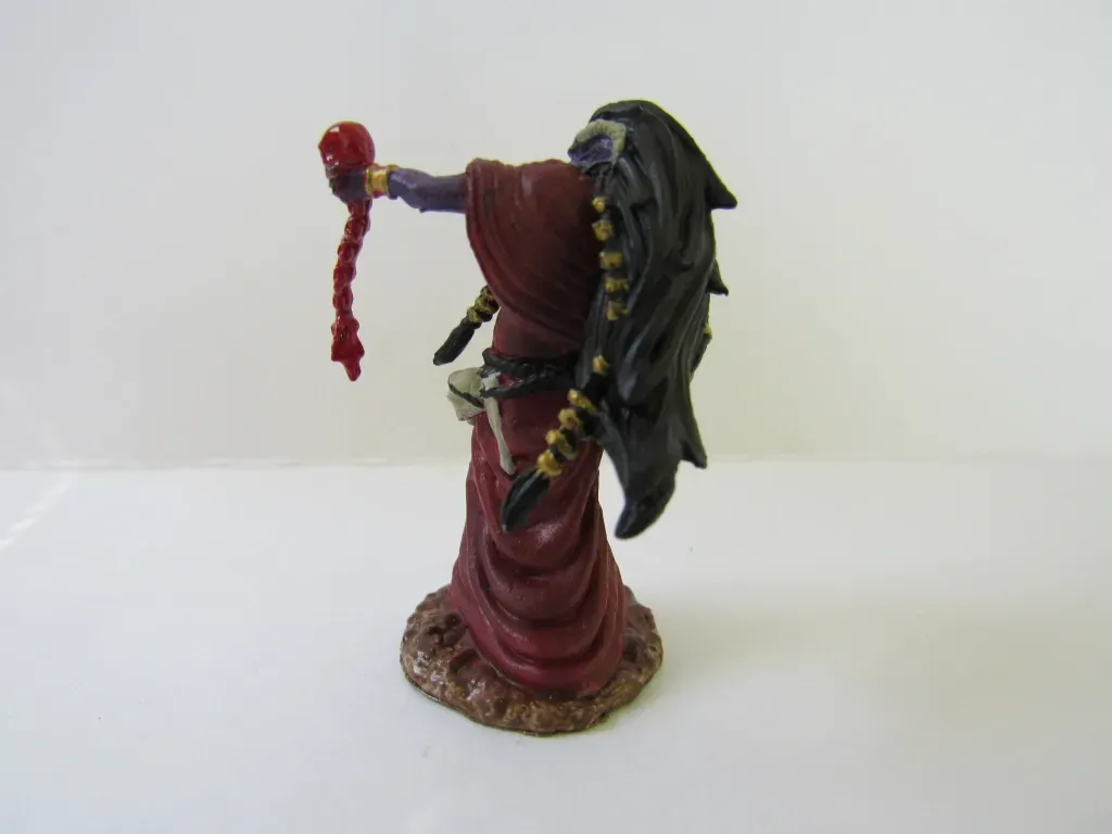 Miniature figure of a robed figure with long black hair, holding a red object.