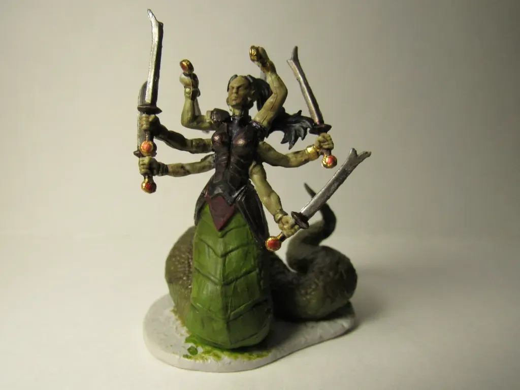 Six-armed, snake-bodied figure holding swords. Dark skin, green scaled tail. On a small grey base.