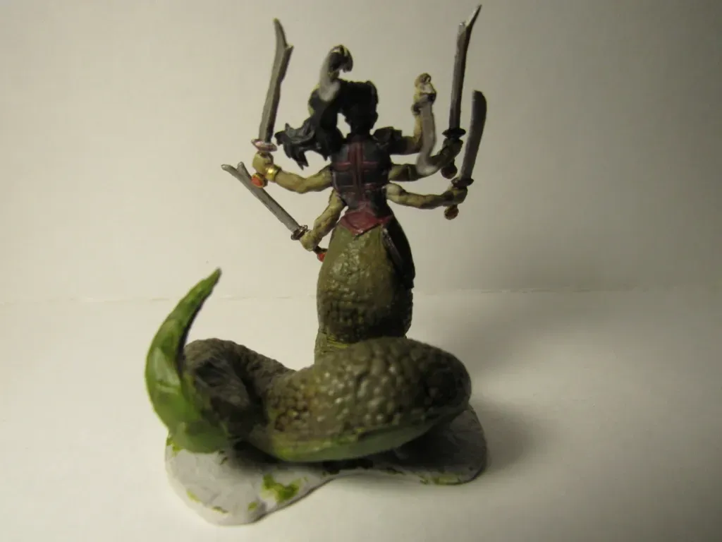 Miniature figurine of a multi-armed warrior with a serpentine body, holding swords, and wearing armor; green and brown.