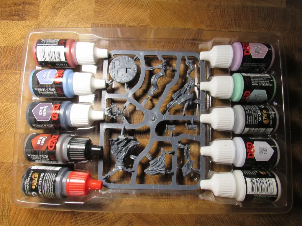 A paint set and unpainted miniatures in a plastic tray. Paints are various colors.