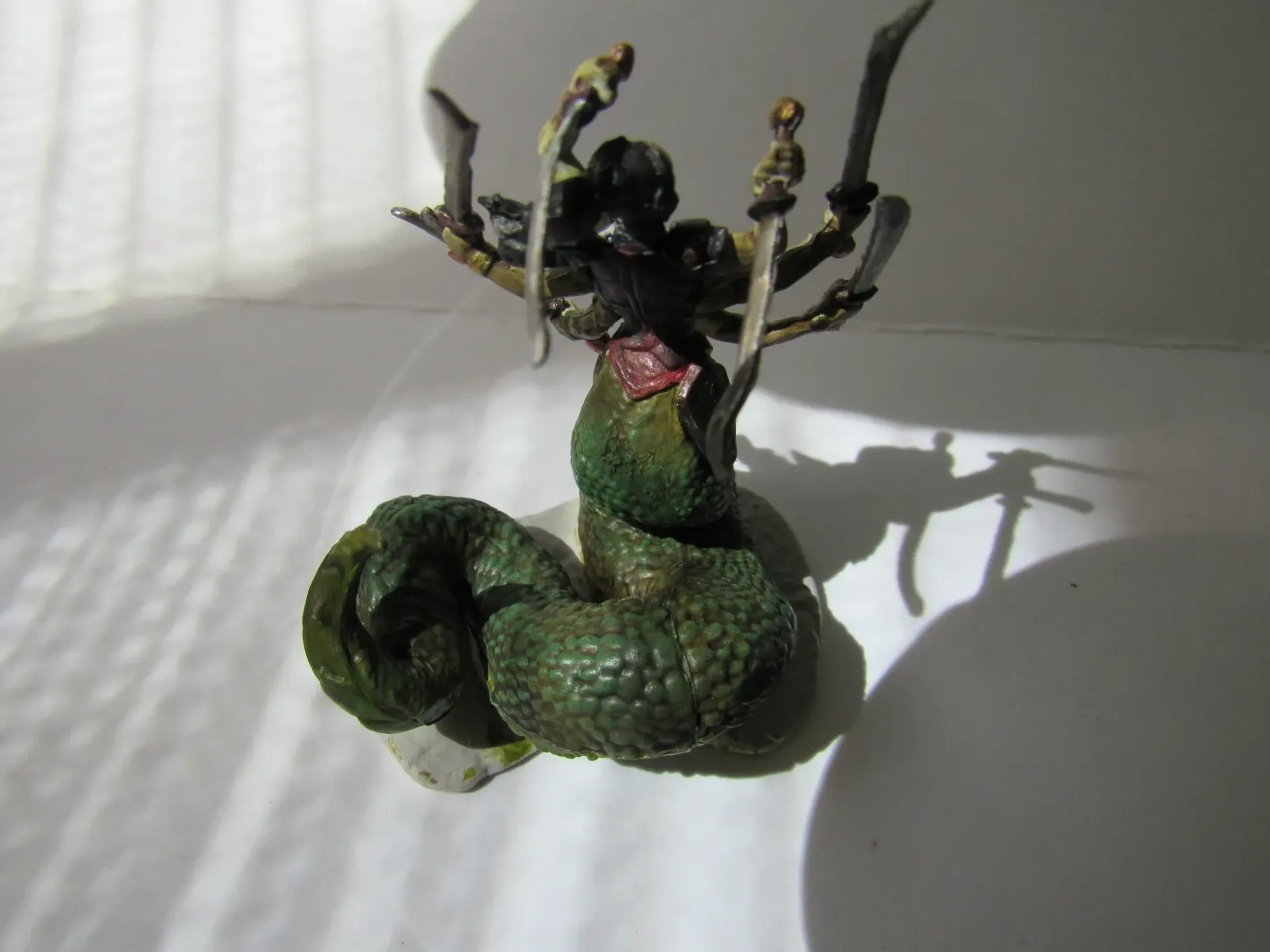 Miniature figure of a green snake-like body with a humanoid upper body holding swords.