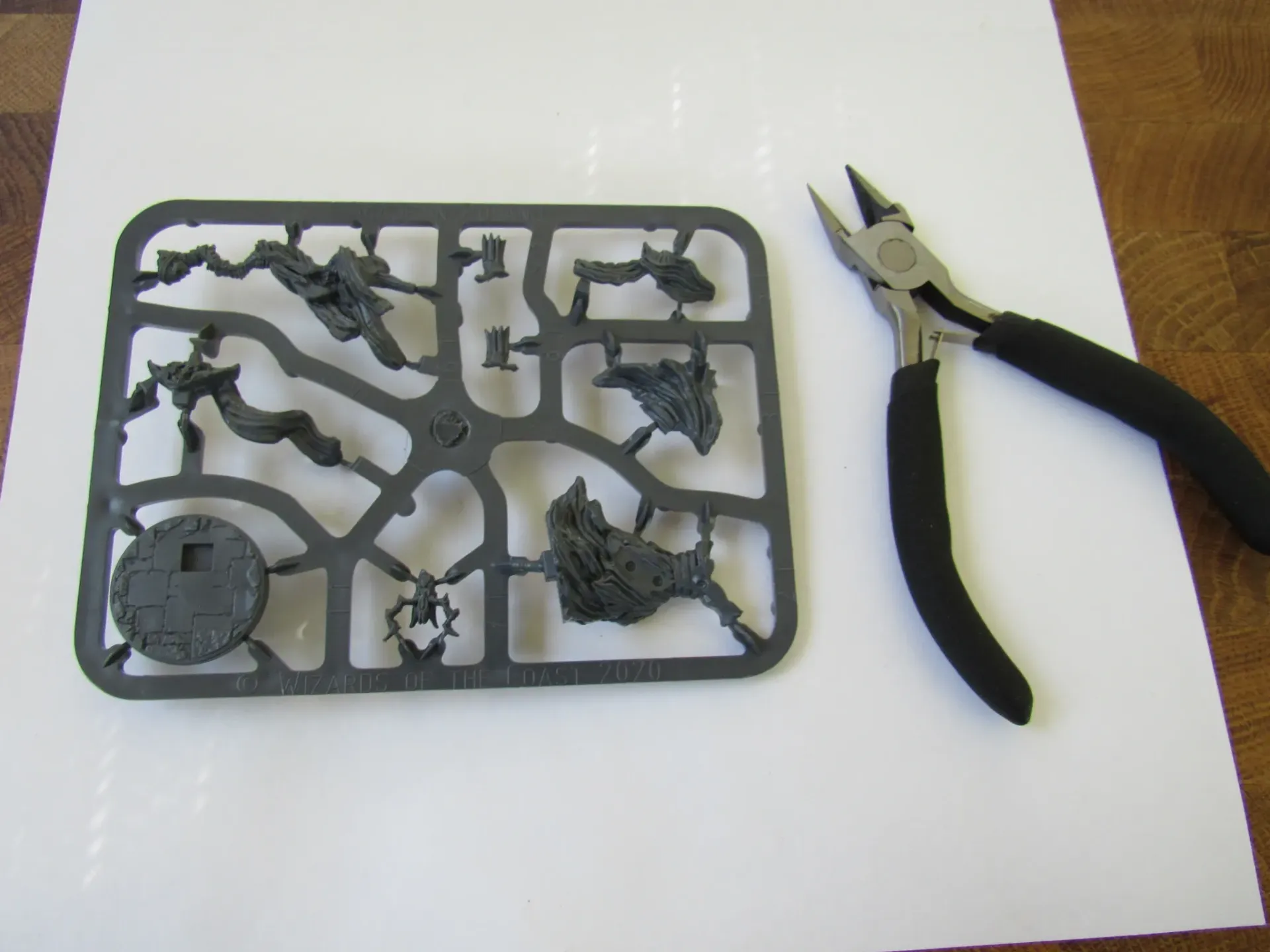 Sprue with miniature parts next to black-handled wire cutters on white paper.