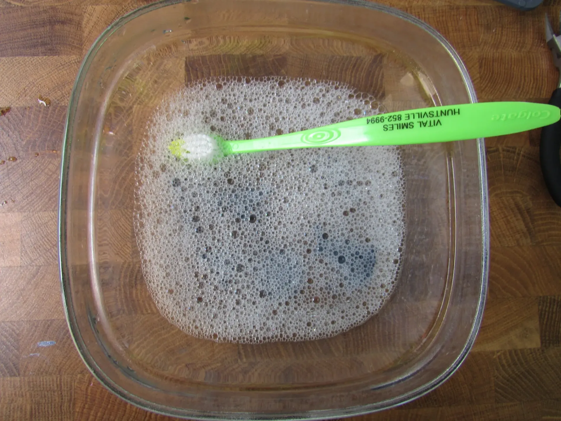 Glass bowl with soapy water and a green toothbrush.