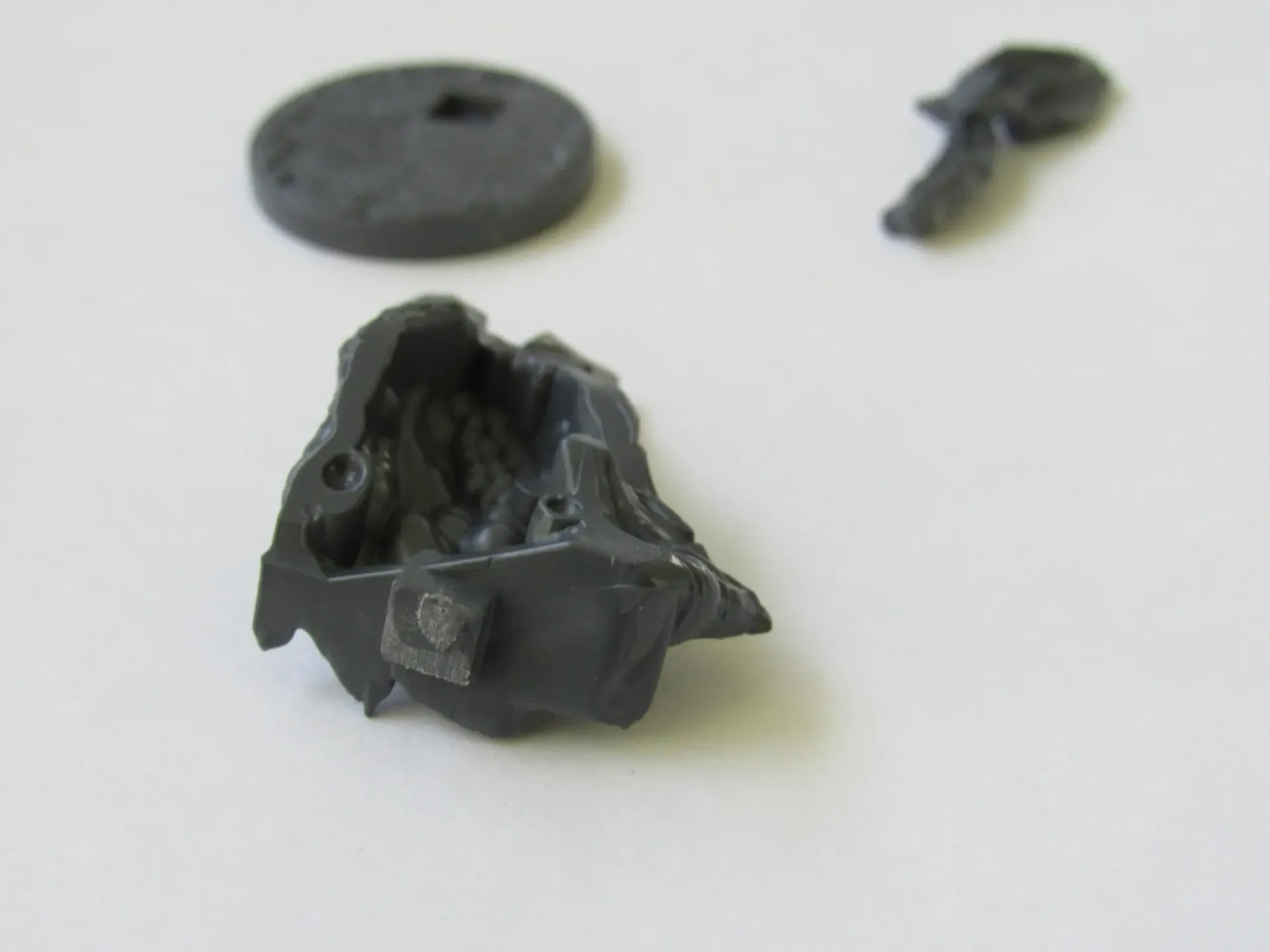 Close-up of four broken dark gray plastic pieces scattered on a white surface.