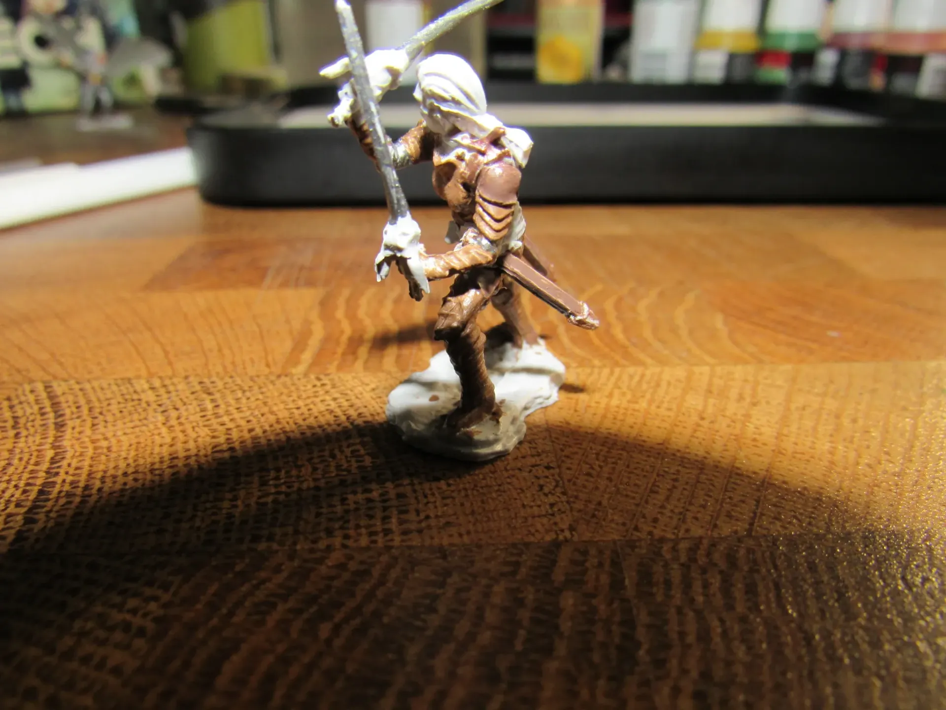 Miniature figure of a warrior with a sword and bow, painted brown and white, standing on a base.