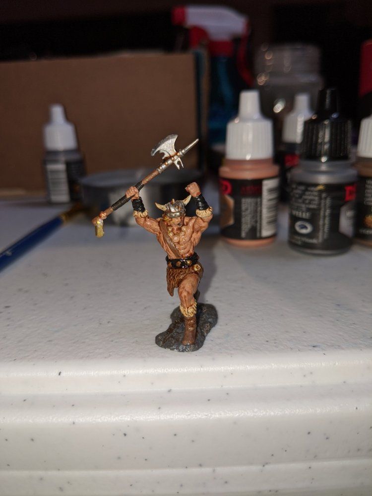 A painted barbarian miniature on a table with a background of paint bottles and painting tools