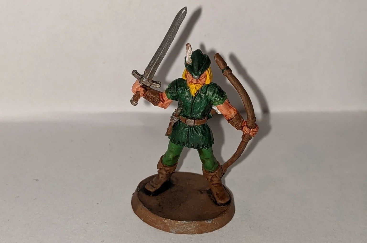 Miniature figure of an archer with sword. Green tunic, brown boots, blonde hair, and a brown base.