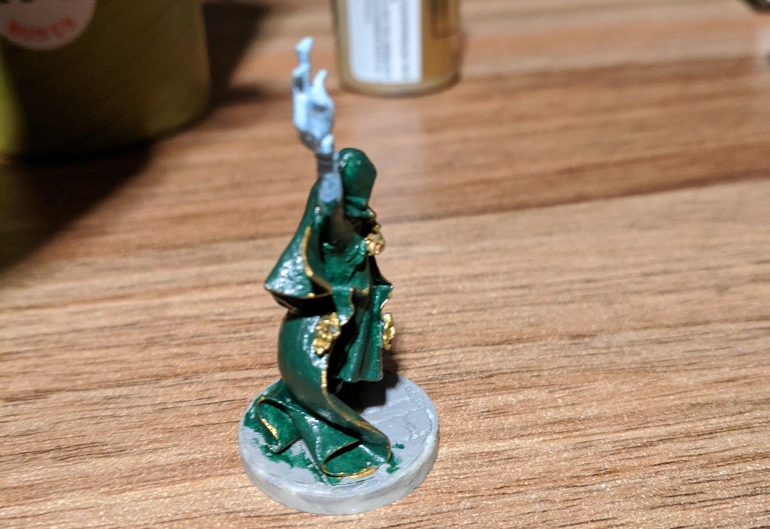 Miniature figurine of a cloaked figure, green robes with gold trim, blue spectral hand, on a gray base.