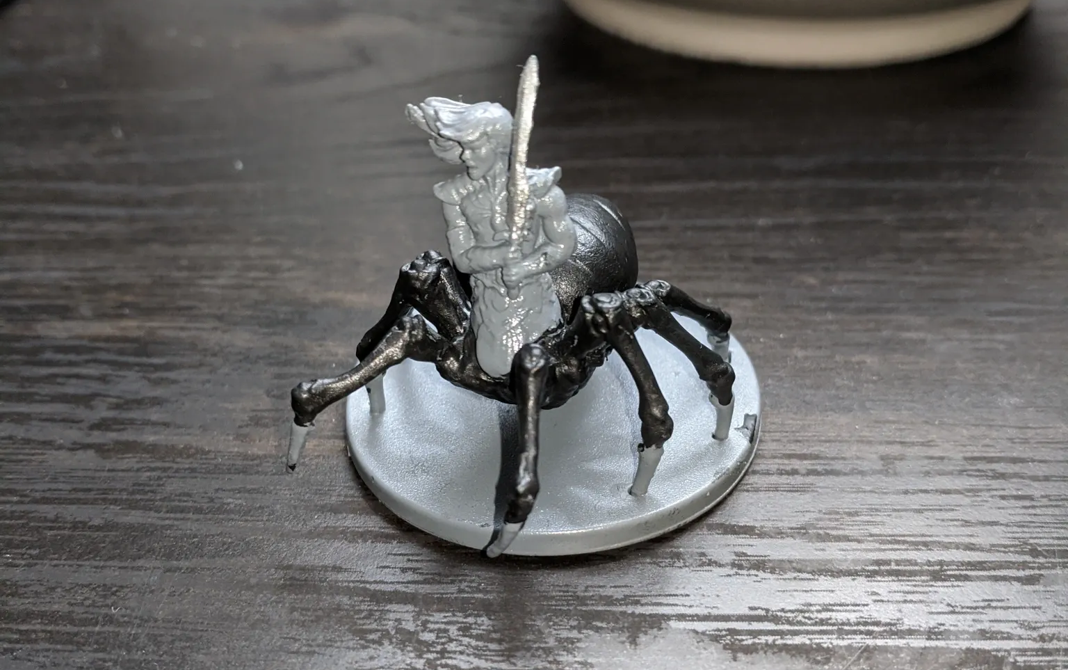Miniature spider with rider, black legs and gray body, on a gray-painted base.