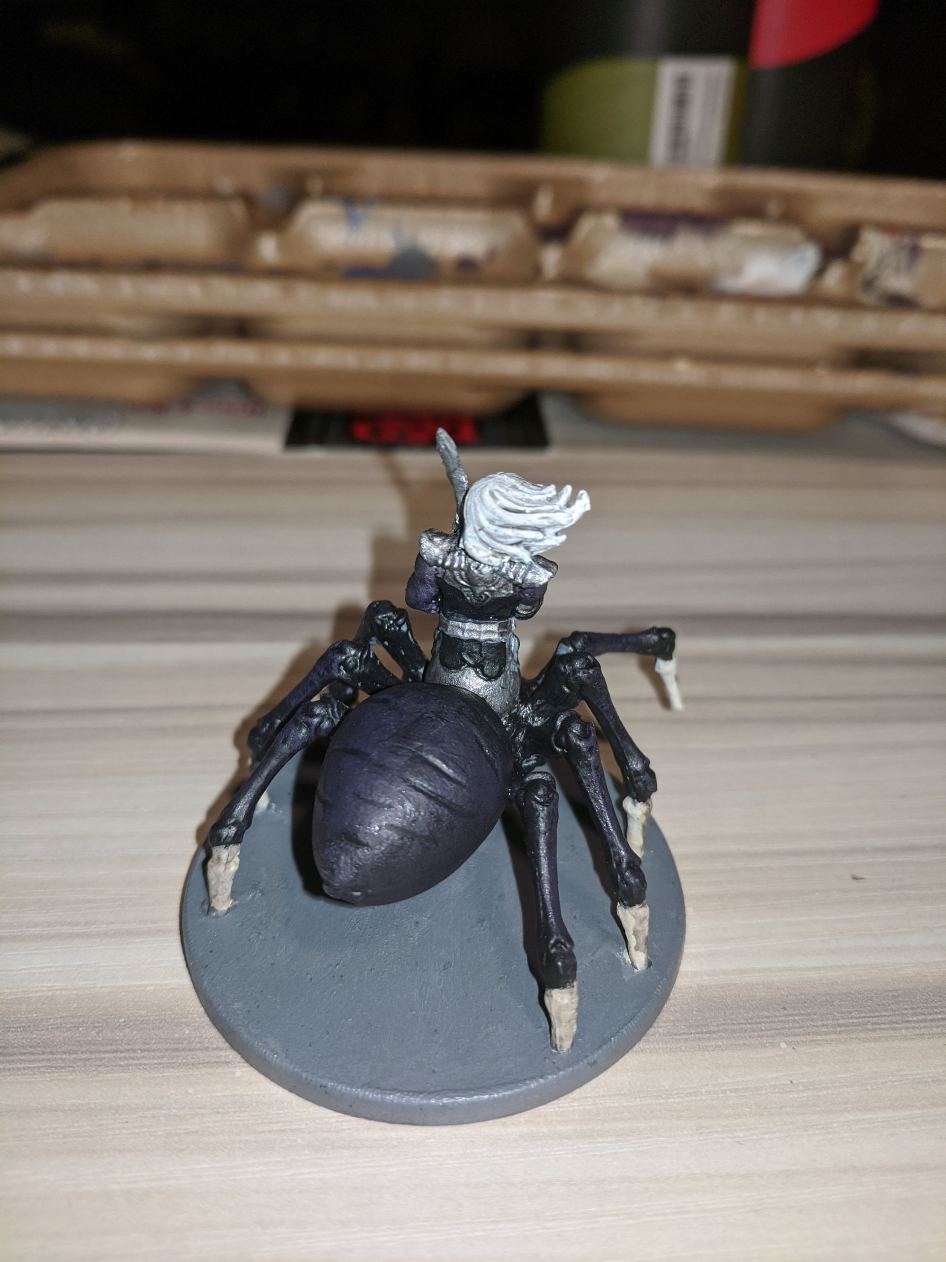 Miniature of a woman with white hair riding a black spider, on a gray circular base.