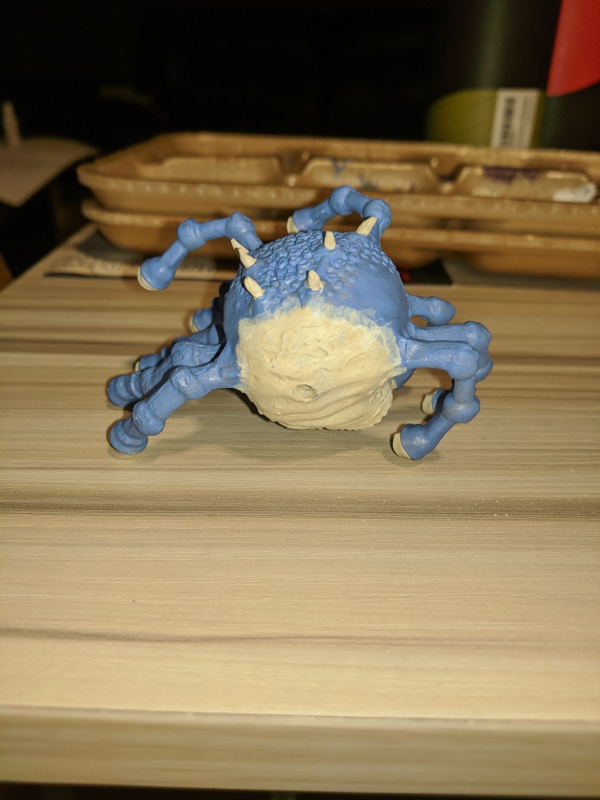 Blue and tan creature with many legs and spikes, on a wooden surface.