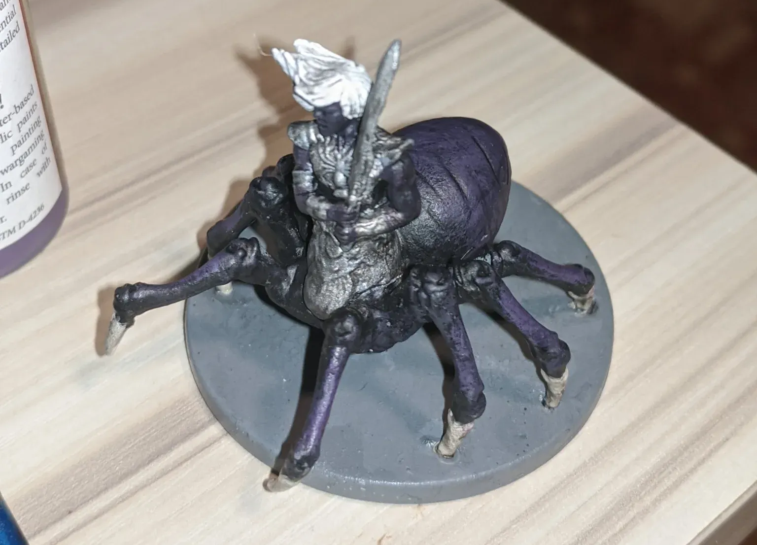 Miniature figure of a spider-like creature with a rider, painted in shades of purple, gray, and white.